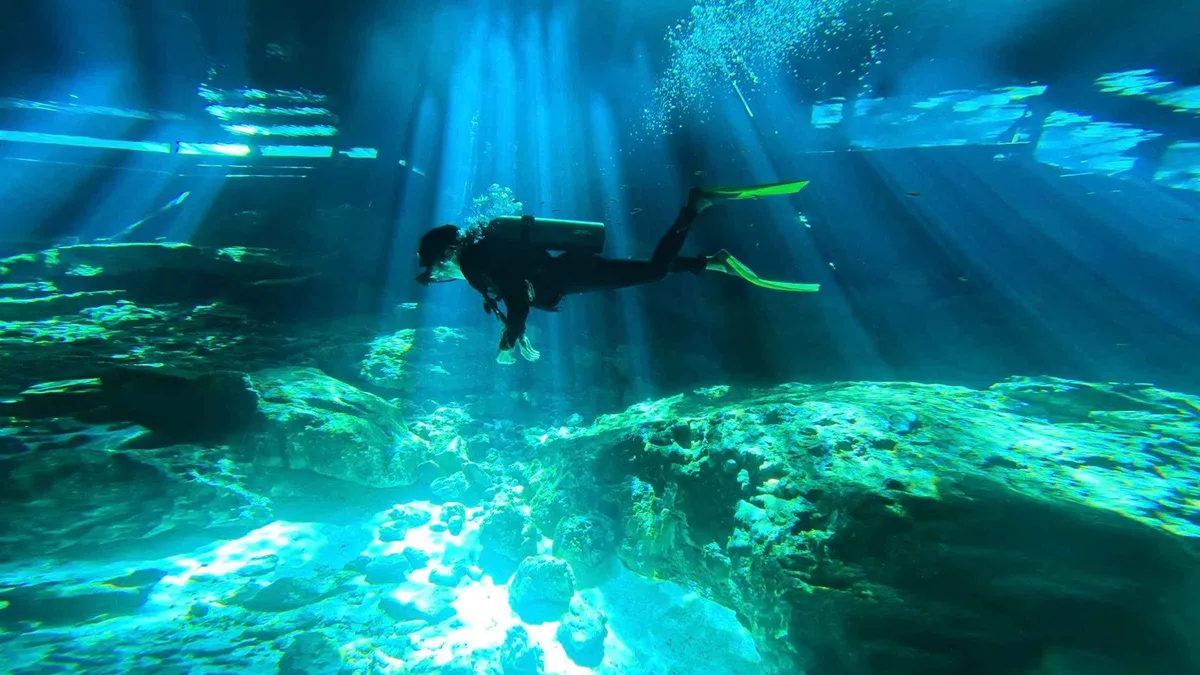 A scuba diver in the light beams of the Dos Ojos cavern on a cenote diving tour near Tulum