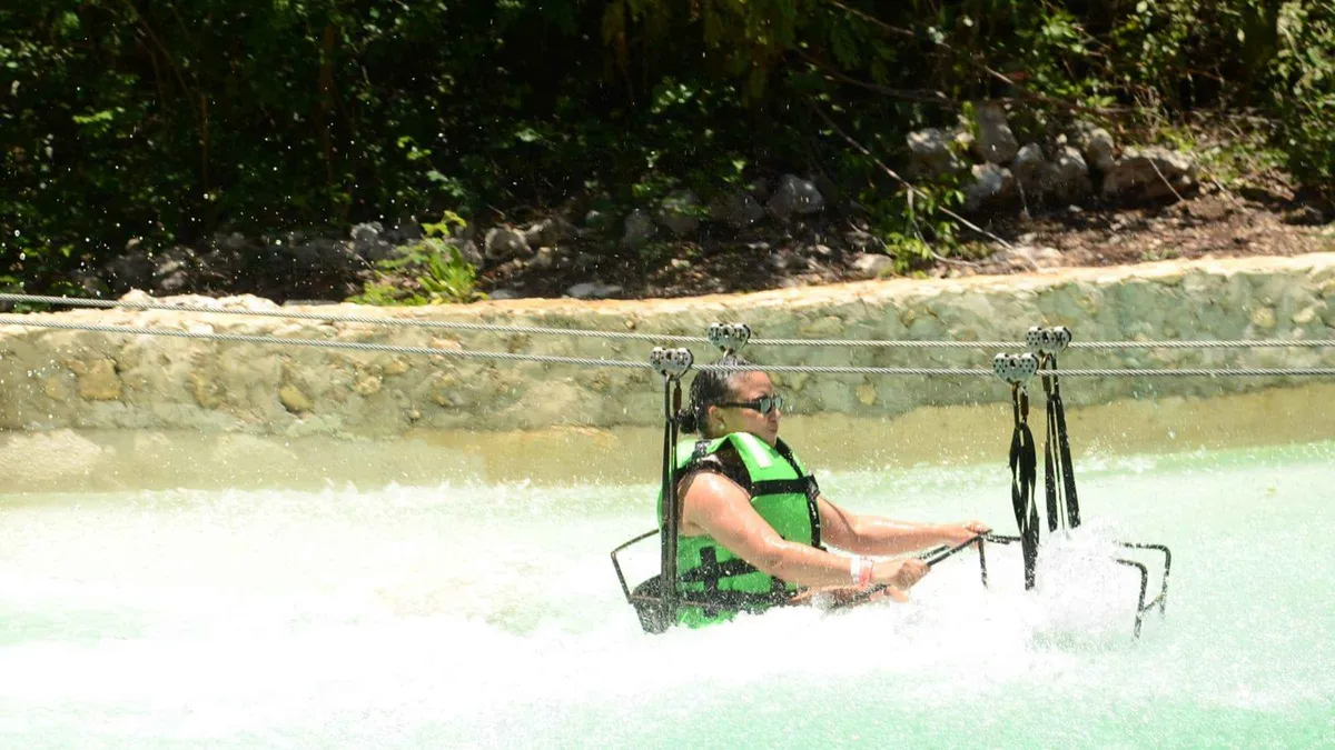 A zipline rider skimming a jungle river before a cave cenote rappel on a Tulum cenote adventure tour